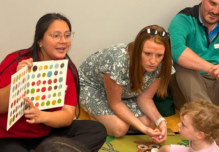 Teacher holding book with colors, pointing at one and showing it to kids